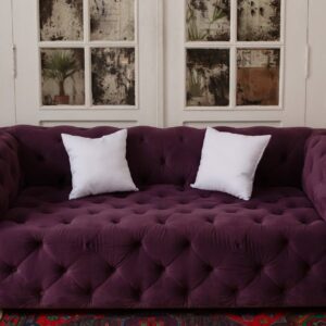 Luxurious purple tufted sofa with white cushions in a stylish, cozy indoor setting.
