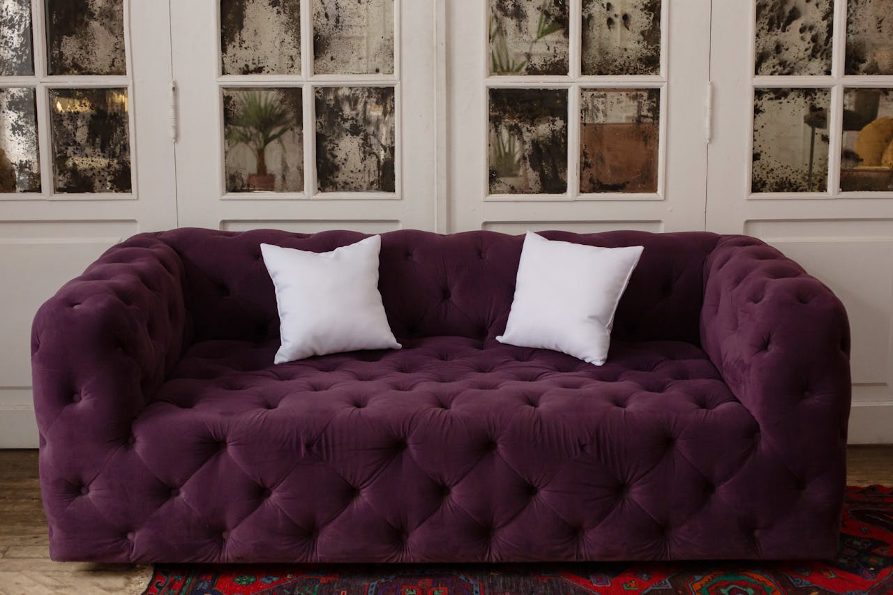 Home Luxurious purple tufted sofa with white cushions in a stylish, cozy indoor setting.